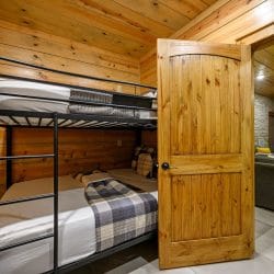 Metal bunk bed with plaid bedding seen through the open bunk room door