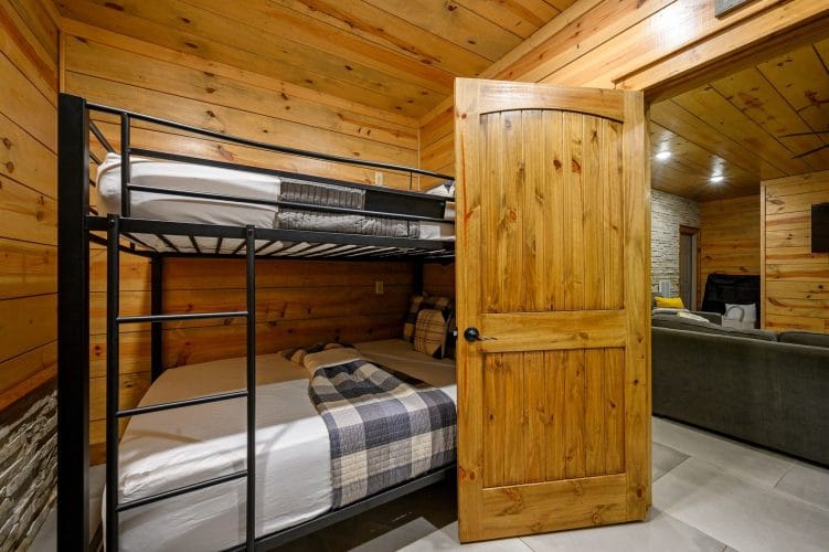Metal bunk bed with plaid bedding seen through the open bunk room door