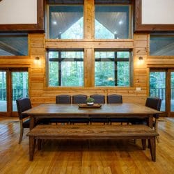Long wood dining table with a bench, in front of tall windows and glass doors