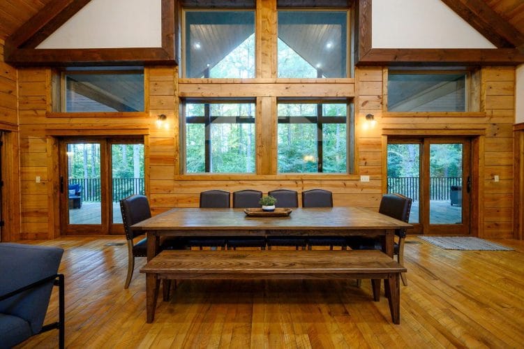 Long wood dining table with a bench, in front of tall windows and glass doors