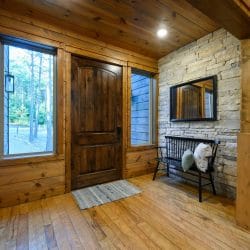Entry with a stained wood door, stone accent wall and a bench