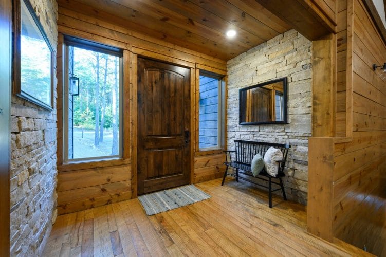 Entry with a stained wood door, stone accent wall and a bench