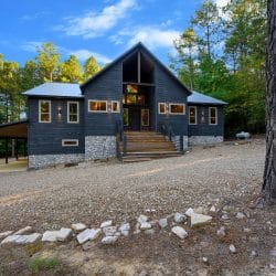 Front of the cabin with a covered carport on the left and pine trees on both sides