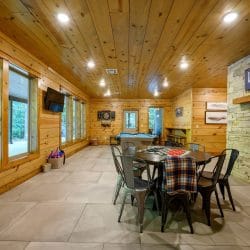 Game room with a round game table, pool table and a stone double-sided fireplace with a Lake Life sign