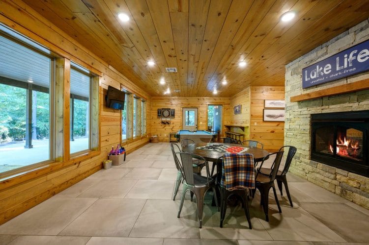 Game room with a round game table, pool table and a stone double-sided fireplace with a Lake Life sign