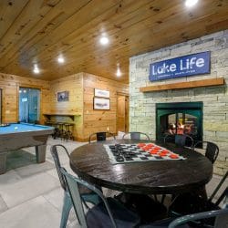 Blue-felt pool table and a round checkers table beside the stone fireplace