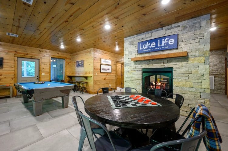 Blue-felt pool table and a round checkers table beside the stone fireplace