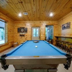 Blue-felt pool table with a dartboard and a row of bar stools along the wall