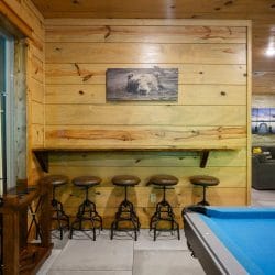 Bar-height shelf with five stools along the wall beside the pool table