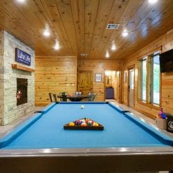 Racked pool table with the stone fireplace beyond and a TV on the wall
