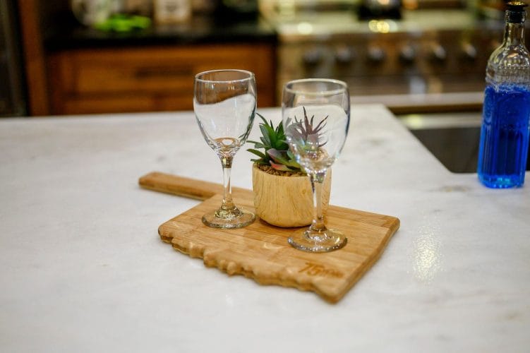 Two wine glasses and a small plant on a cutting board on the kitchen counter