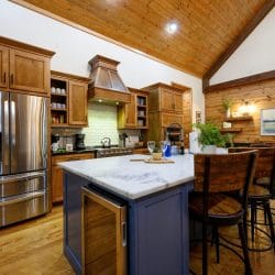 Kitchen with a stainless fridge, navy island with a white top and wood counter stools