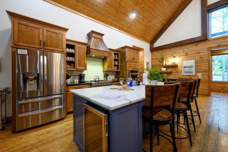Kitchen with a stainless fridge, navy island with a white top and wood counter stools