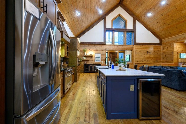 Stainless fridge and navy island with the great room behind
