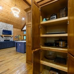 Open pantry cabinet holding small appliances, with the living room beyond