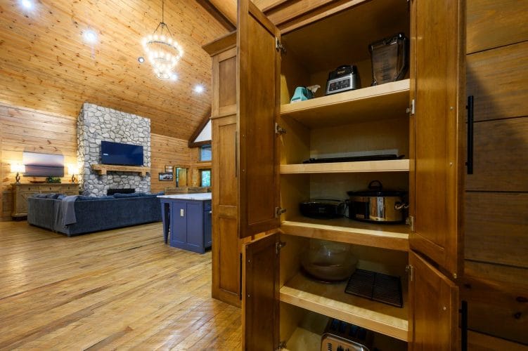Open pantry cabinet holding small appliances, with the living room beyond