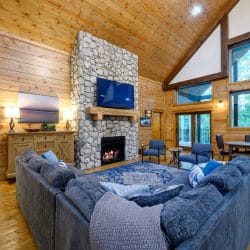 Great room with a tall stone fireplace, wall-mounted TV and a big gray sectional