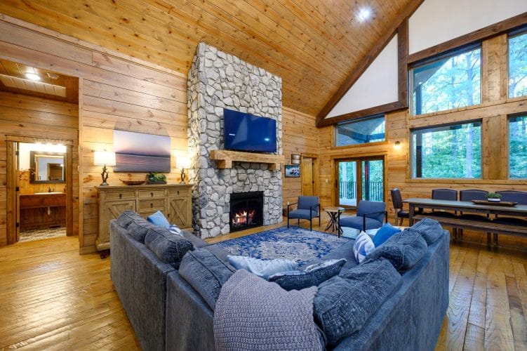 Great room with a tall stone fireplace, wall-mounted TV and a big gray sectional