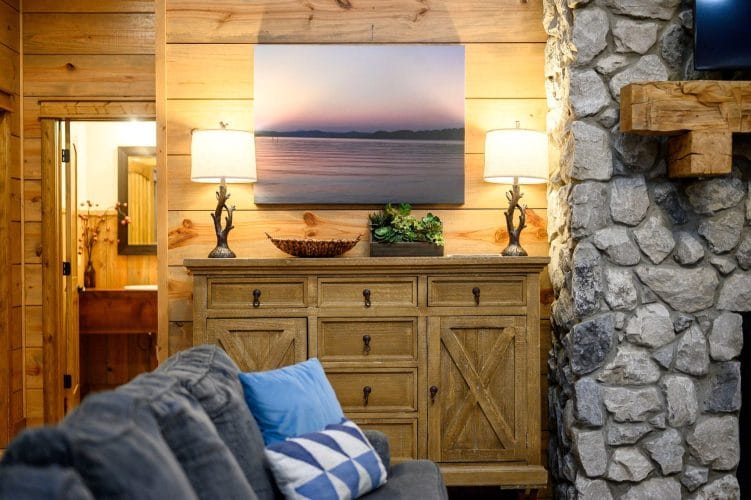 Wood sideboard under a framed lake photo, beside the stone fireplace