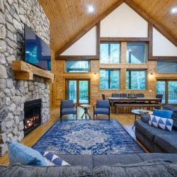 Living room under a vaulted wood ceiling with a blue rug and sectional, dining table in the back
