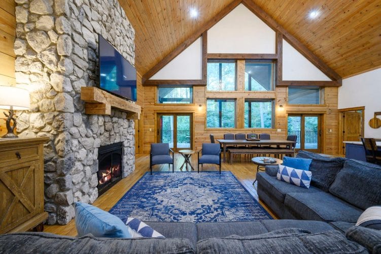 Living room under a vaulted wood ceiling with a blue rug and sectional, dining table in the back