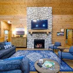 Stone fireplace with a TV above, sectional and blue chairs on a patterned rug