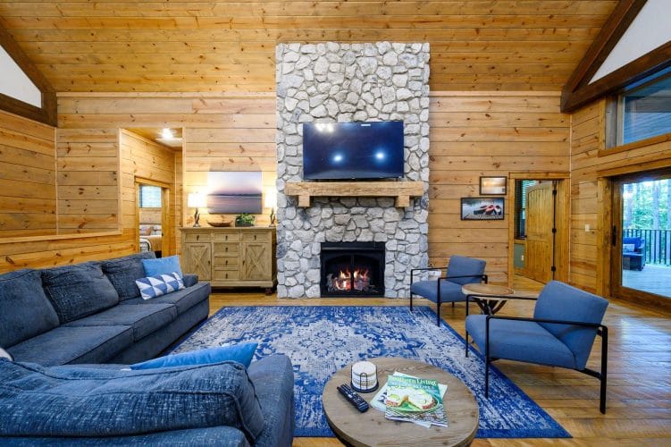 Stone fireplace with a TV above, sectional and blue chairs on a patterned rug