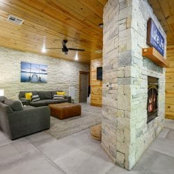 Lower-level sitting area with gray chairs and an ottoman, split by the stone fireplace