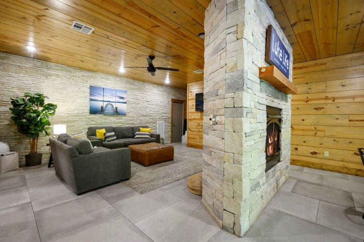 Lower-level sitting area with gray chairs and an ottoman, split by the stone fireplace