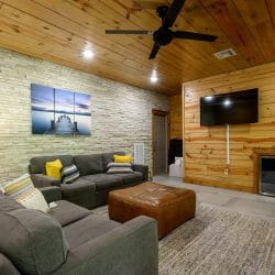 Lower-level living area with gray sofas, a leather ottoman and a wall-mounted TV