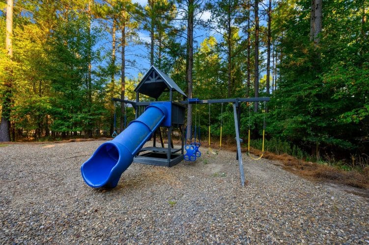 Playset with a blue slide and swings on a gravel play area