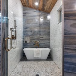 Freestanding soaking tub beside a glass shower with blue-veined tile