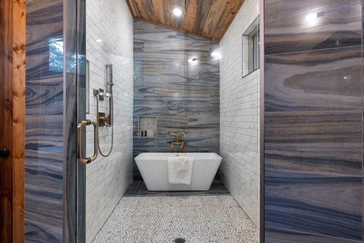 Freestanding soaking tub beside a glass shower with blue-veined tile