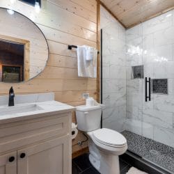 Bathroom with a round mirror, a white vanity and a marble-look shower
