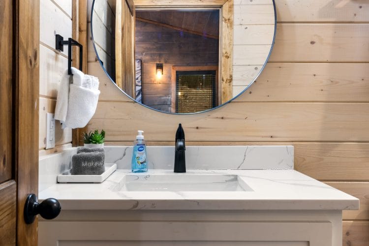 White vanity with a round mirror, the bedroom reflected behind