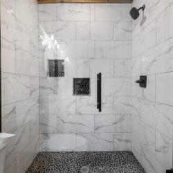 Marble-look tiled walk-in shower with a black rain head