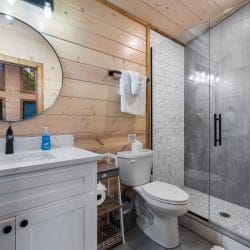 Bathroom with a round mirror, a white vanity and a gray-tile shower