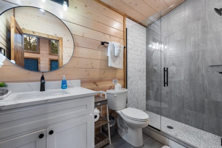 Bathroom with a round mirror, a white vanity and a gray-tile shower