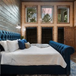 King bed with a navy tufted frame and white bedding under a row of tall windows