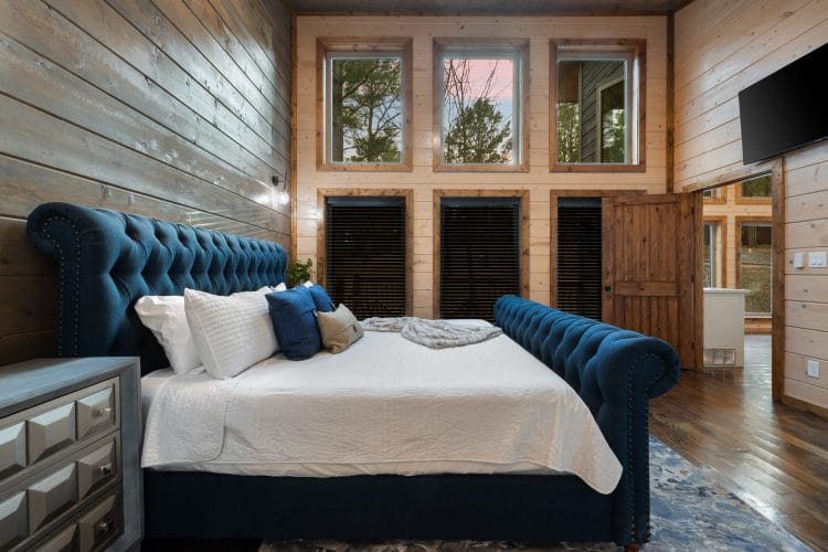 King bed with a navy tufted frame and white bedding under a row of tall windows