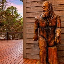 Carved wooden Bigfoot statue standing on the deck beside the cabin wall