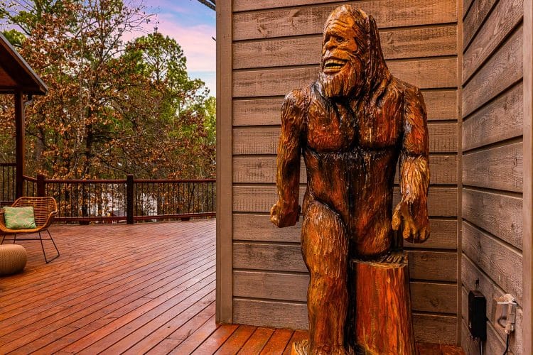 Carved wooden Bigfoot statue standing on the deck beside the cabin wall