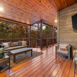 Covered deck with an outdoor sofa and chairs and a big TV on the wall