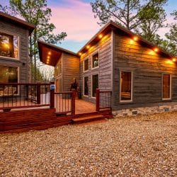 Back of the main house and game house with a large reddish deck and lights at dusk