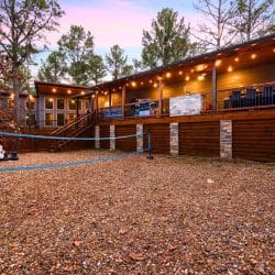 Back of the cabin with a long lit deck, a volleyball net and giant chess on the gravel