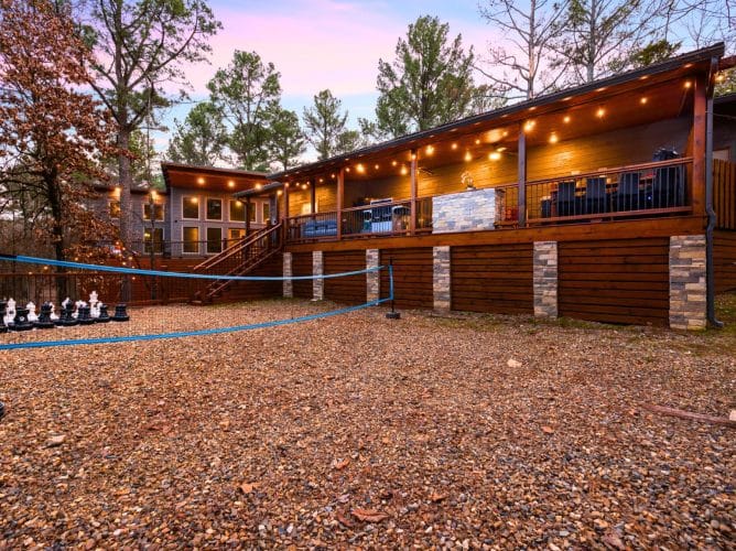 Back of the cabin with a long lit deck, a volleyball net and giant chess on the gravel
