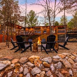 Stone-ringed fire pit with Adirondack chairs and the lit house behind