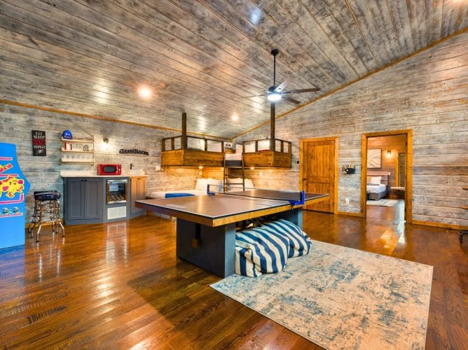 Game house with a ping pong table, an arcade cabinet, a bunk loft above and a kitchenette against a gray wood wall