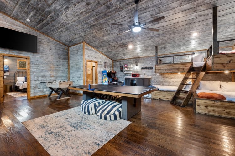 Game house with a ping pong table, foosball, arcade cabinets and a bunk loft under a gray wood ceiling