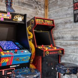 Two arcade cabinets with stools beside a wall sign